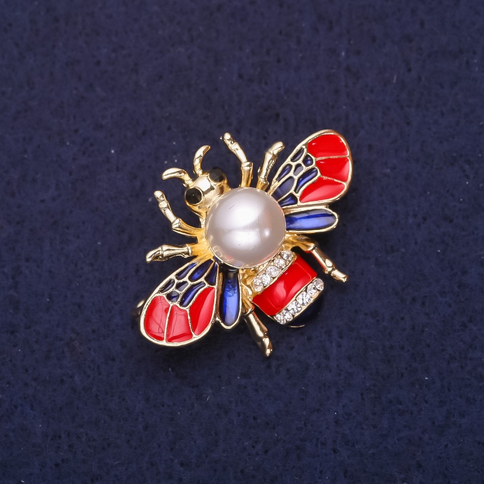 Brožka Včela se perlovou korálkou, štrasami a smaltem, barvy červená, modrá a bílá, 35×25 mm, zlatistý kov